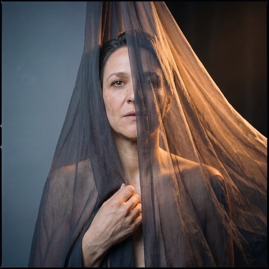 A woman's face half-veiled behind sheer fabric